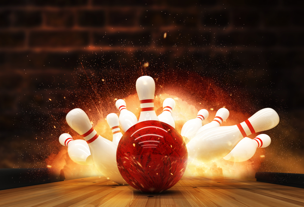 A red bowling ball explodes into a row of bowling pins.