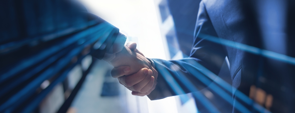 Two businesspeople shake hands in front of a bright window