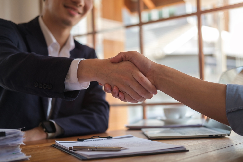 Two business people shake hands over paperwork.